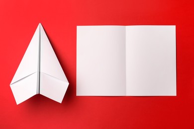Photo of Handmade white plane and folded piece of paper on red background, flat lay