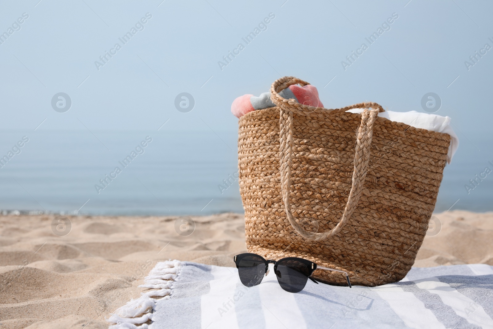 Photo of Beach bag, towels, sunglasses and blanket on sandy seashore, space for text