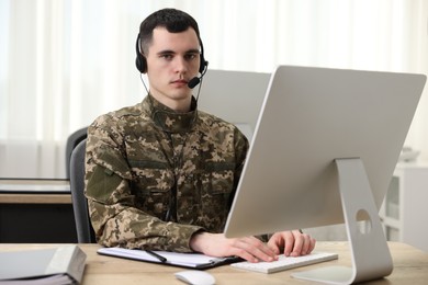 Photo of Military service. Young soldier in headphones working with computer at table in office