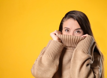 Photo of Young woman in stylish brown sweater on yellow background, space for text
