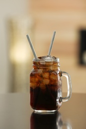 Photo of Mason jar of cola with ice on table against blurred background