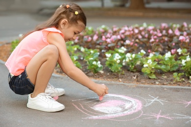 Photo of Little child drawing heart with chalk on asphalt