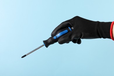 Photo of Woman holding screwdriver on light blue background, closeup