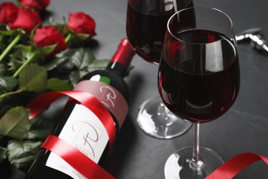 Photo of Bottle and glasses of red wine near beautiful roses on black table, closeup
