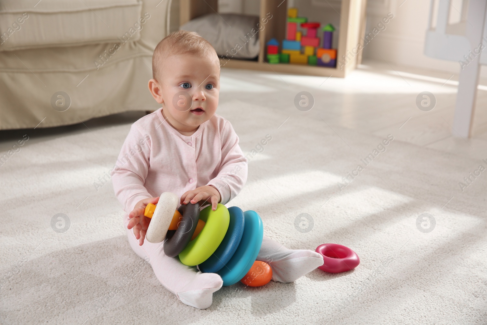 Photo of Cute baby girl playing with toy pyramid on floor at home