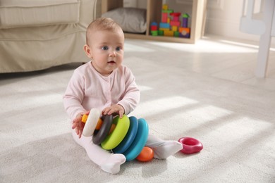 Cute baby girl playing with toy pyramid on floor at home