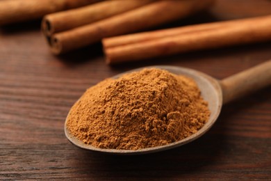 Spoon with cinnamon powder and sticks on wooden table, closeup