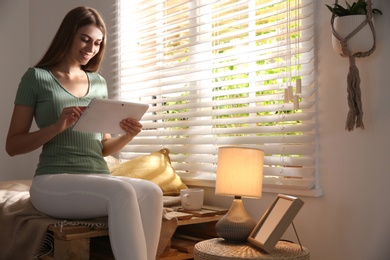 Photo of Beautiful young woman using tablet near window at home
