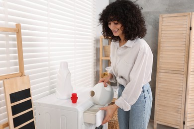 Photo of Woman pouring laundry detergent into washing machine indoors