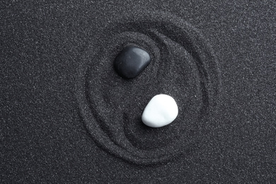Photo of Yin Yang symbol made with stones on black sand, top view. Zen concept