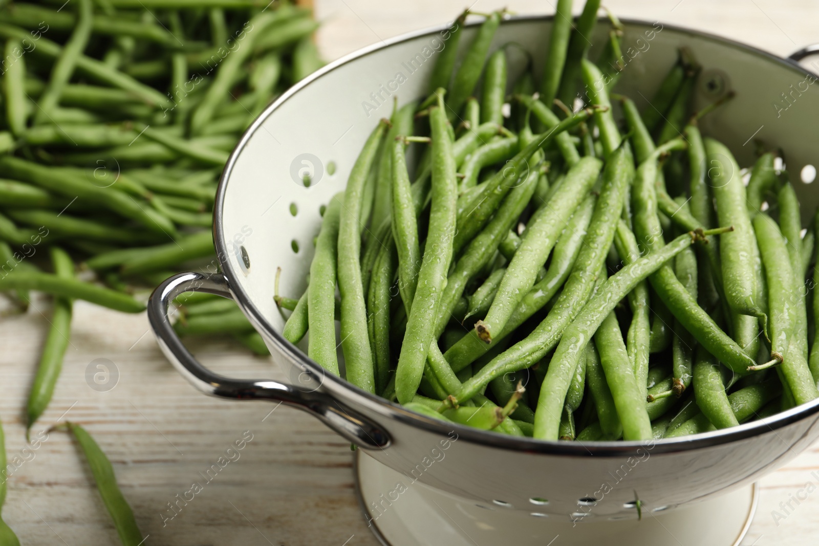 Photo of Fresh green beans in colander on white wooden table, closeup