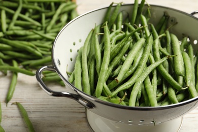 Fresh green beans in colander on white wooden table, closeup