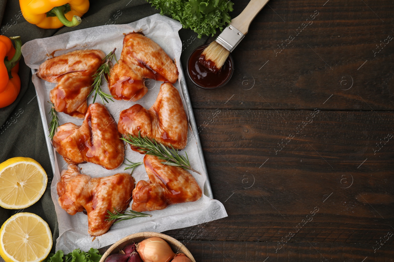 Photo of Flat lay composition with raw marinated chicken wings, rosemary and other products on wooden table. Space for text