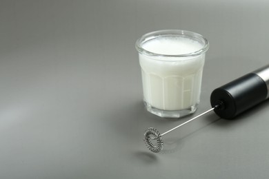 Photo of Mini mixer (milk frother) and whipped milk in glass on grey background. Space for text