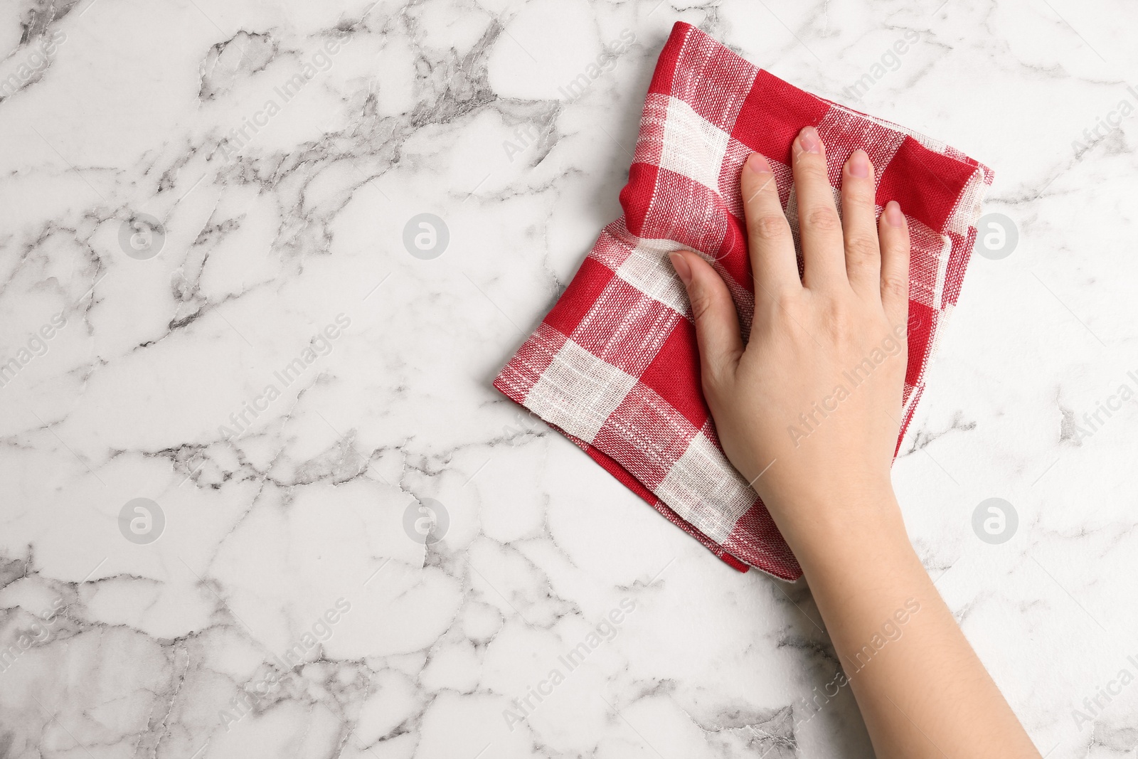 Photo of Woman wiping white marble table with kitchen towel, top view