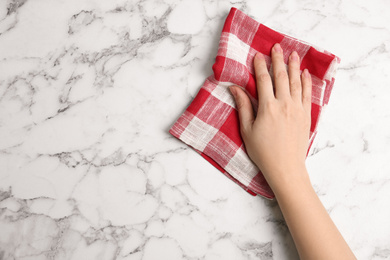 Photo of Woman wiping white marble table with kitchen towel, top view