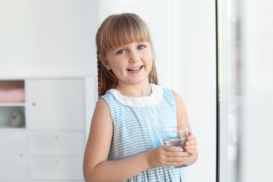 Photo of Cute little girl holding glass of fresh water at home