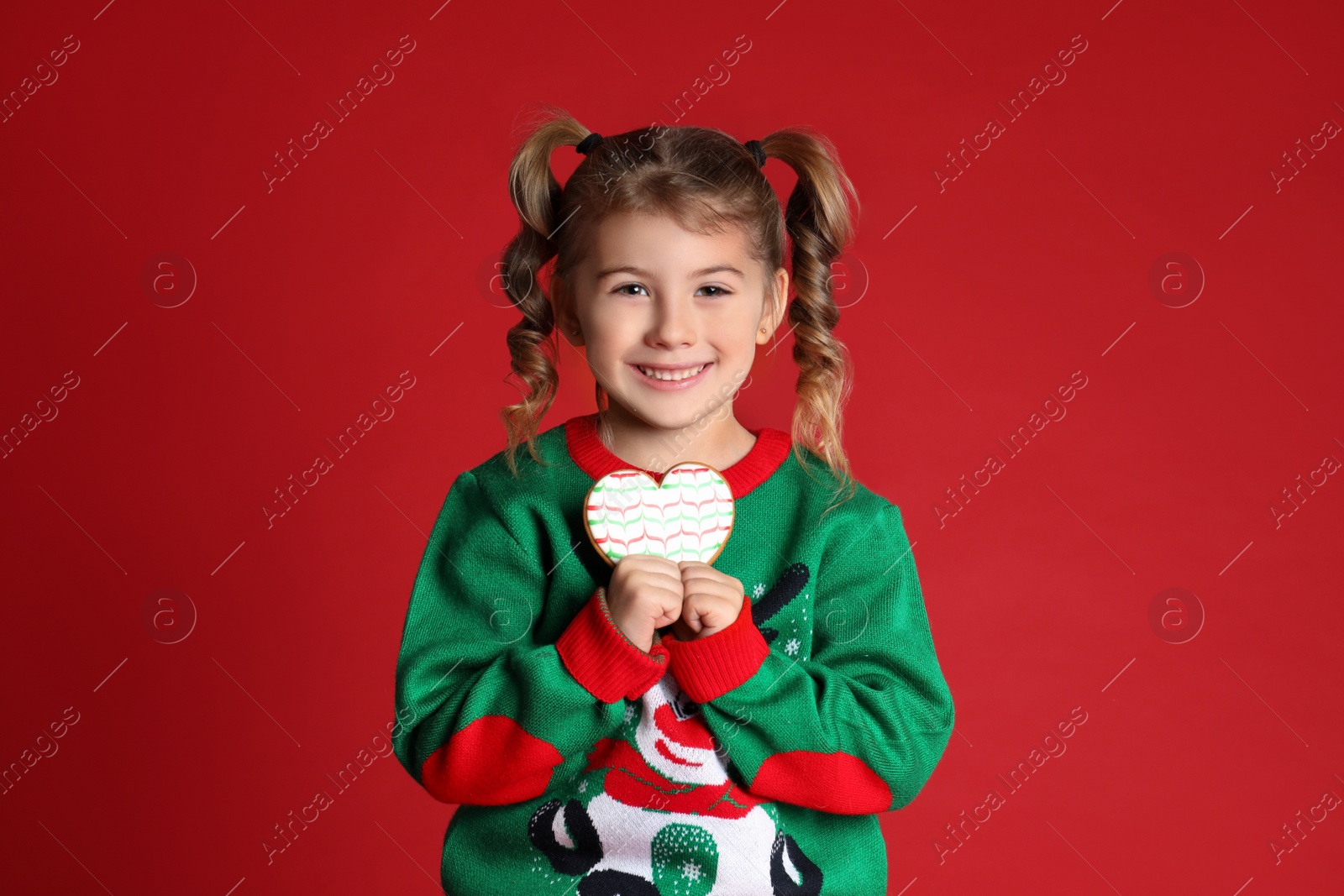 Photo of Cute little girl with Christmas gingerbread cookie on red background