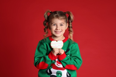 Photo of Cute little girl with Christmas gingerbread cookie on red background