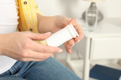 Woman holding bottle of pills indoors, closeup view