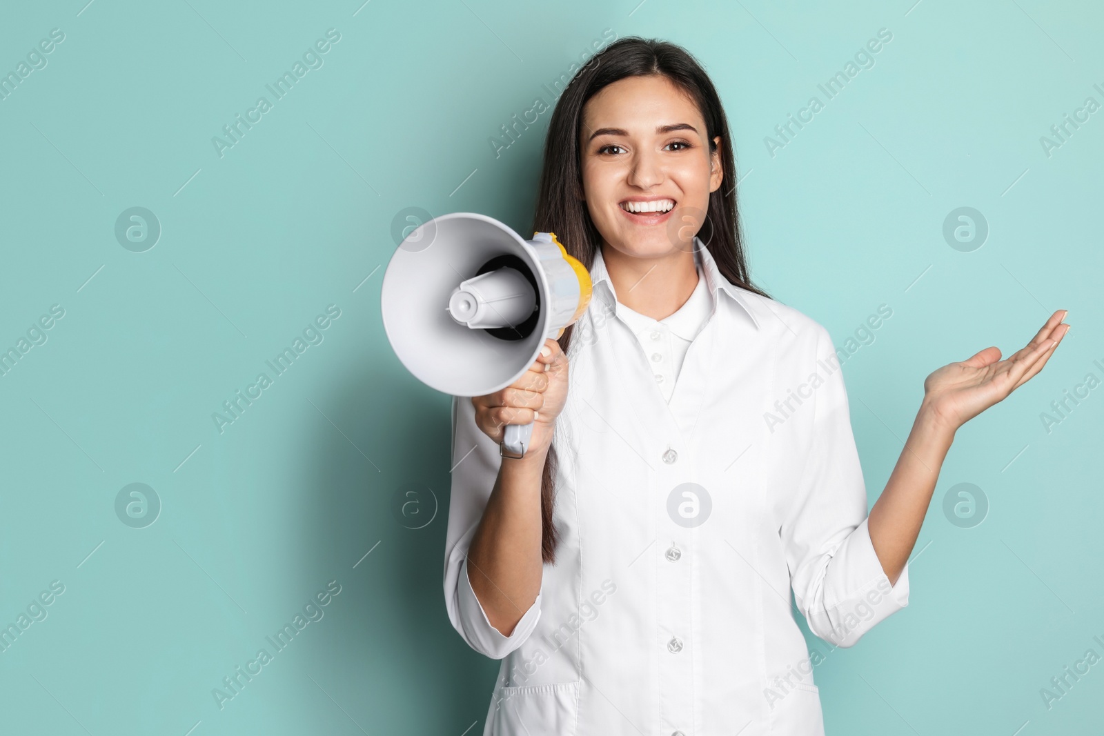 Photo of Young female doctor with megaphone on color background