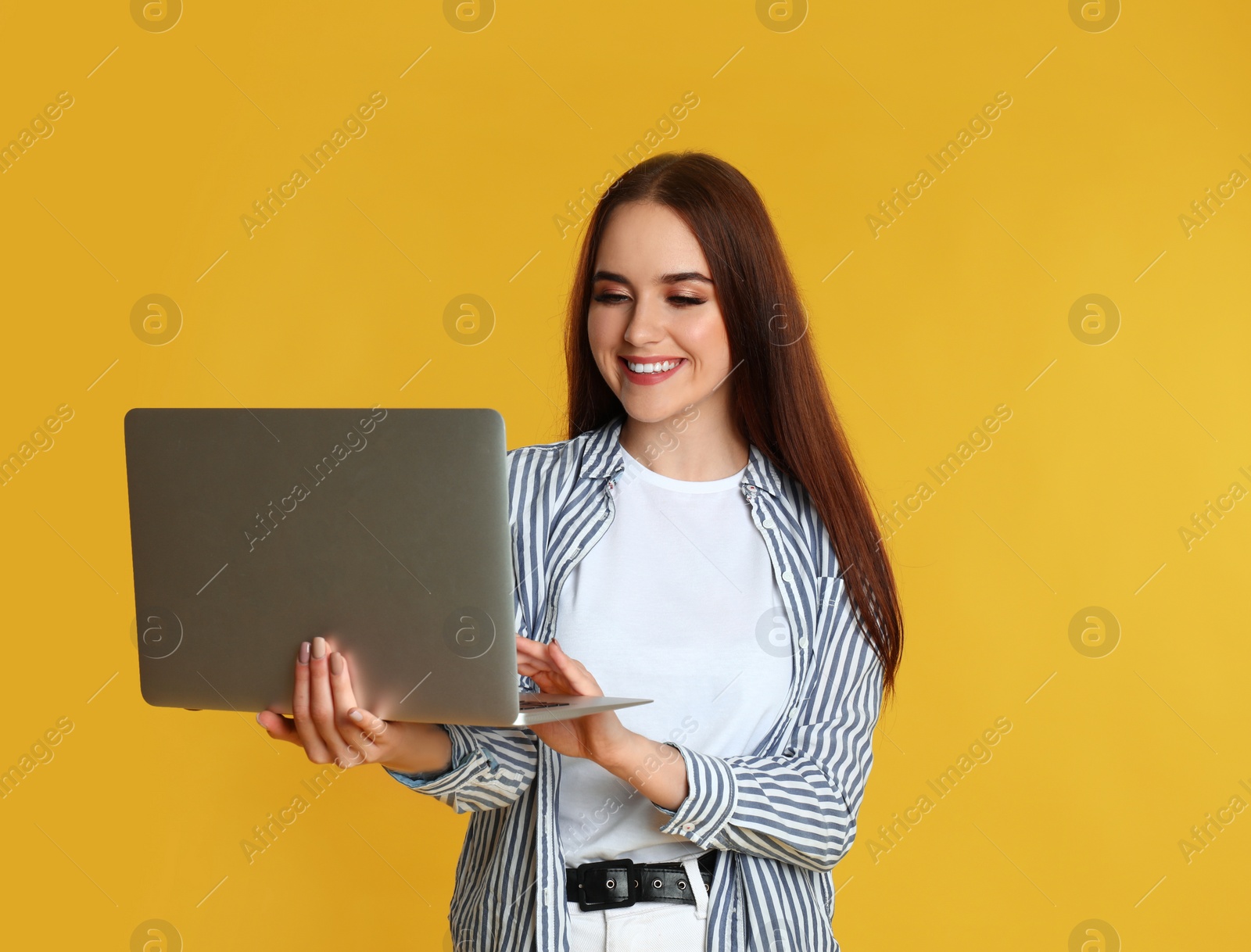 Photo of Happy woman with modern laptop on yellow background