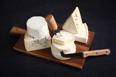 Different types of cheese, knife and fork on black table