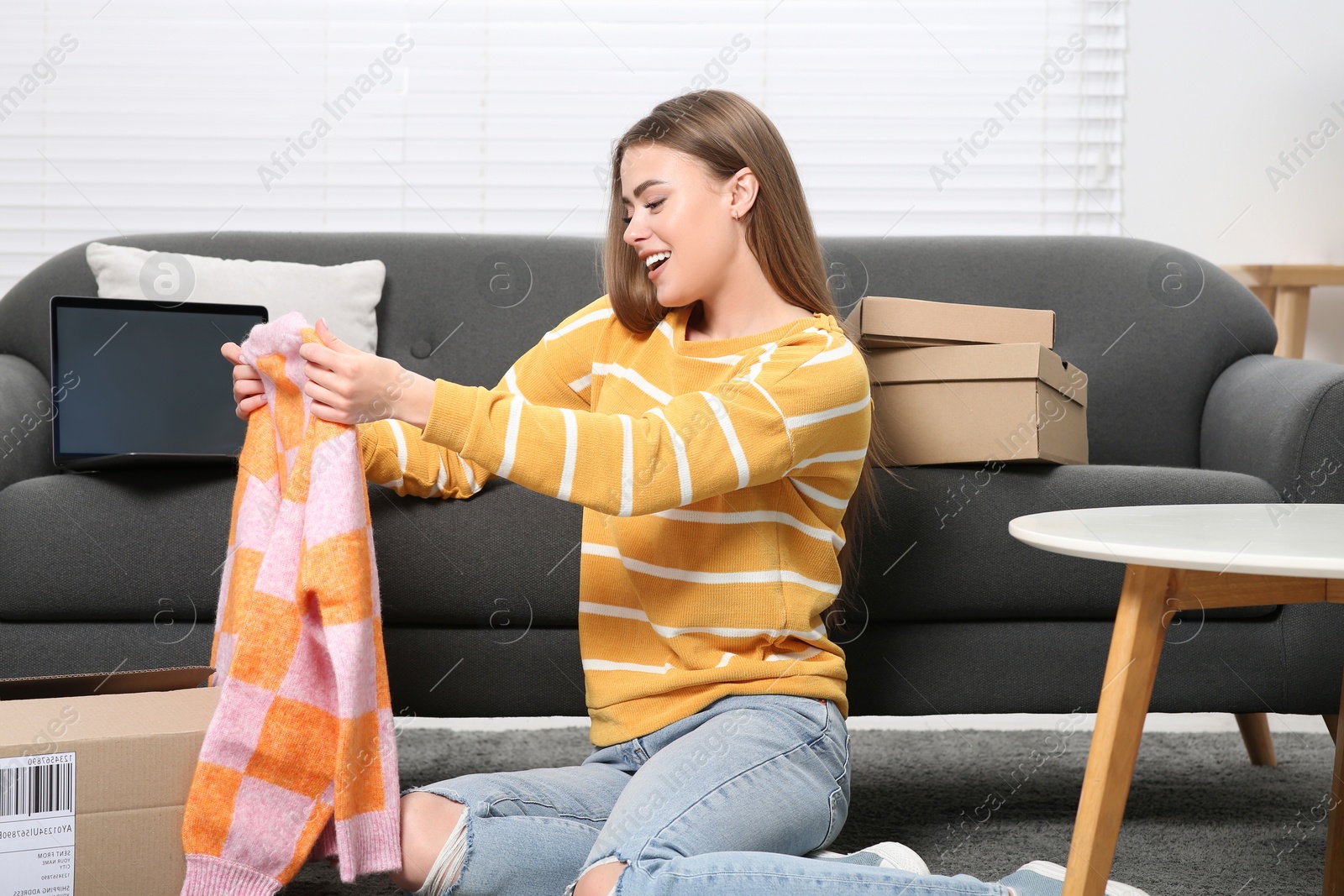 Photo of Happy woman with just unpacked new sweater at home. Online store