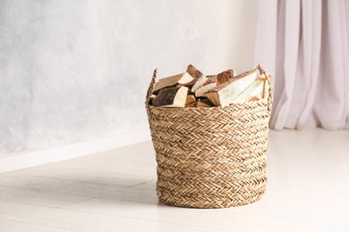 Wicker basket with cut firewood on white floor indoors