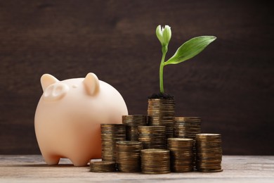 Photo of Stacks of coins with flower and piggy bank on wooden table. Investment concept