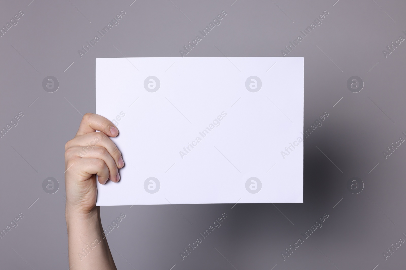 Photo of Woman holding sheet of paper on grey background, closeup. Mockup for design