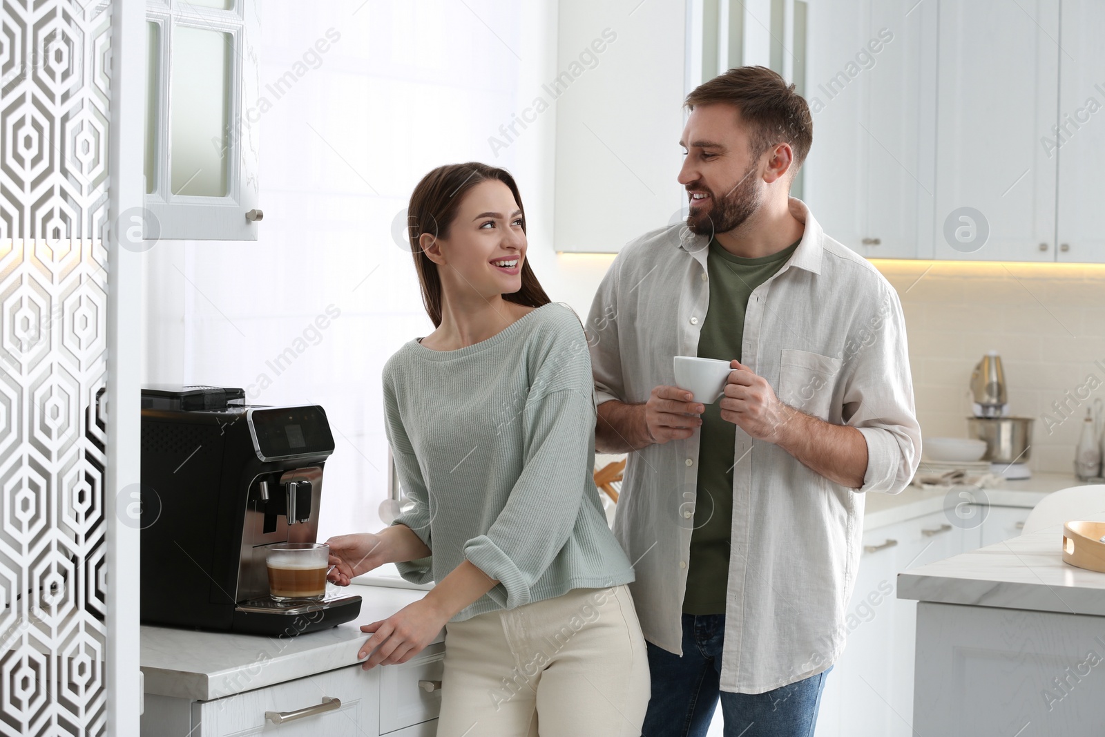 Photo of Happy couple preparing fresh aromatic coffee with modern machine in kitchen