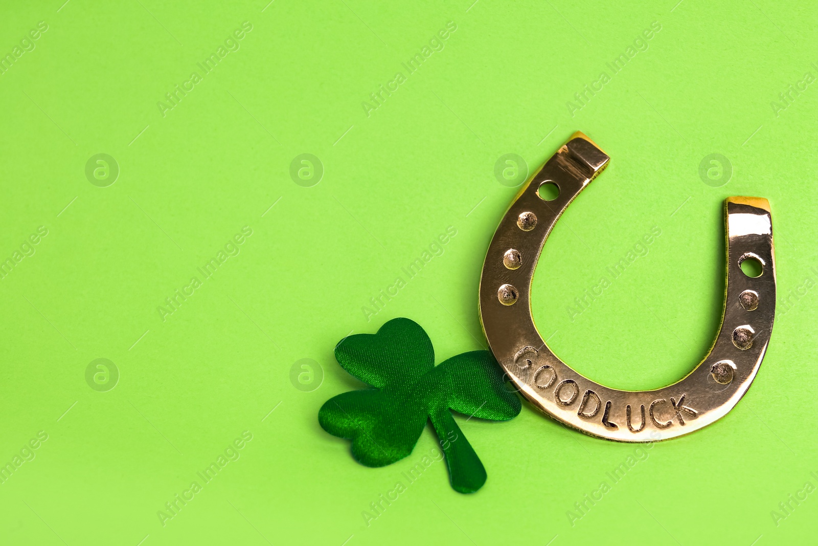 Photo of Golden horseshoe and decorative clover leaf on light green background, space for text. Saint Patrick's Day celebration