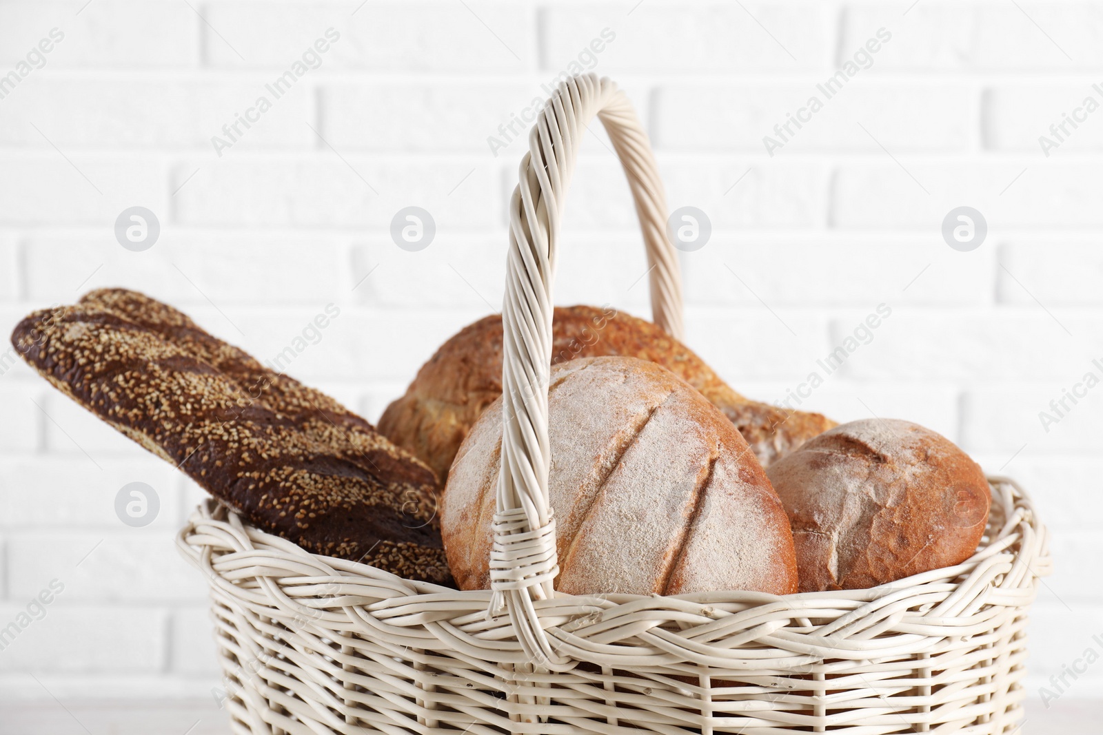 Photo of Different types of bread in wicker basket against white brick wall, closeup