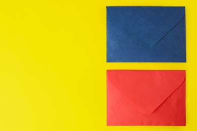 Colorful paper envelopes on yellow background, flat lay. Space for text