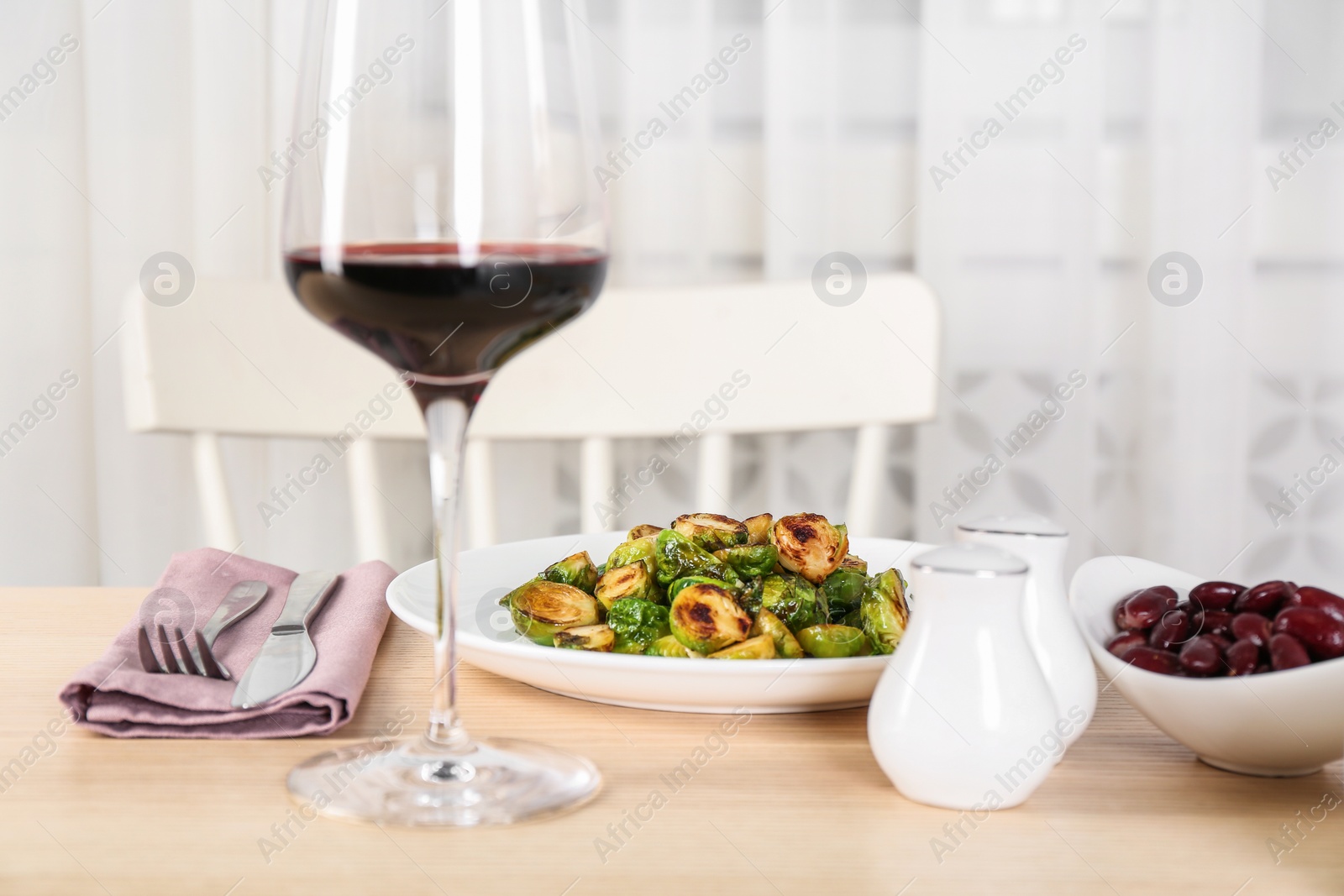 Photo of Delicious roasted Brussels sprouts served with wine and beans on wooden table indoors