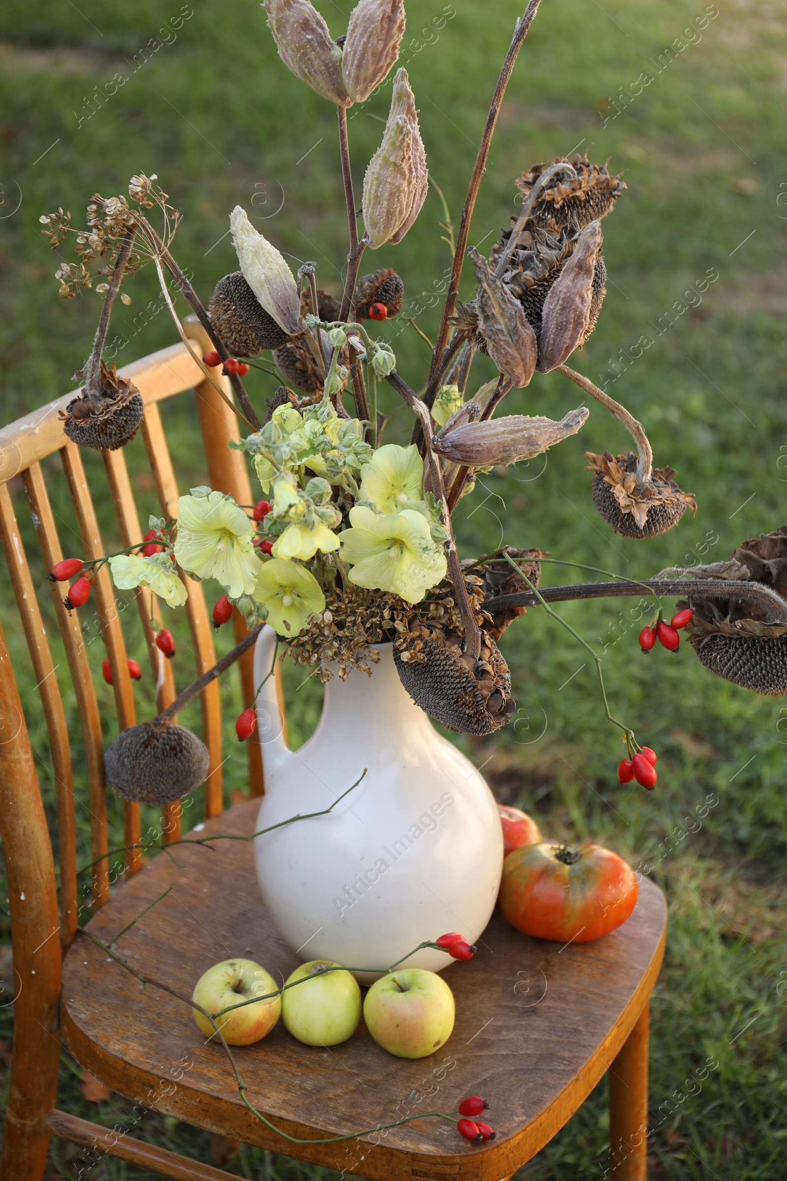 Photo of Composition with beautiful flowers, dry sunflowers and apples on wooden chair outdoors. Autumn atmosphere