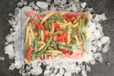 Photo of Zip bag with different frozen vegetables and ice on grey table, top view