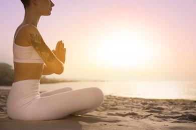 Image of Young woman meditating on beach at sunrise, closeup. Practicing yoga