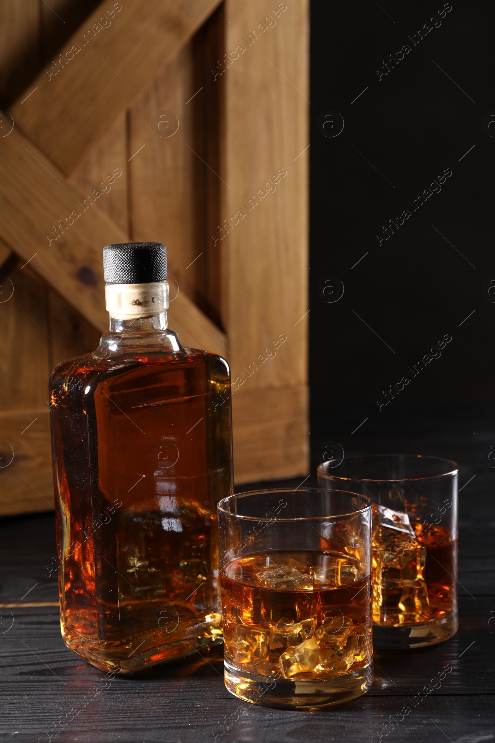 Photo of Whiskey with ice cubes in glasses and bottle on black wooden table