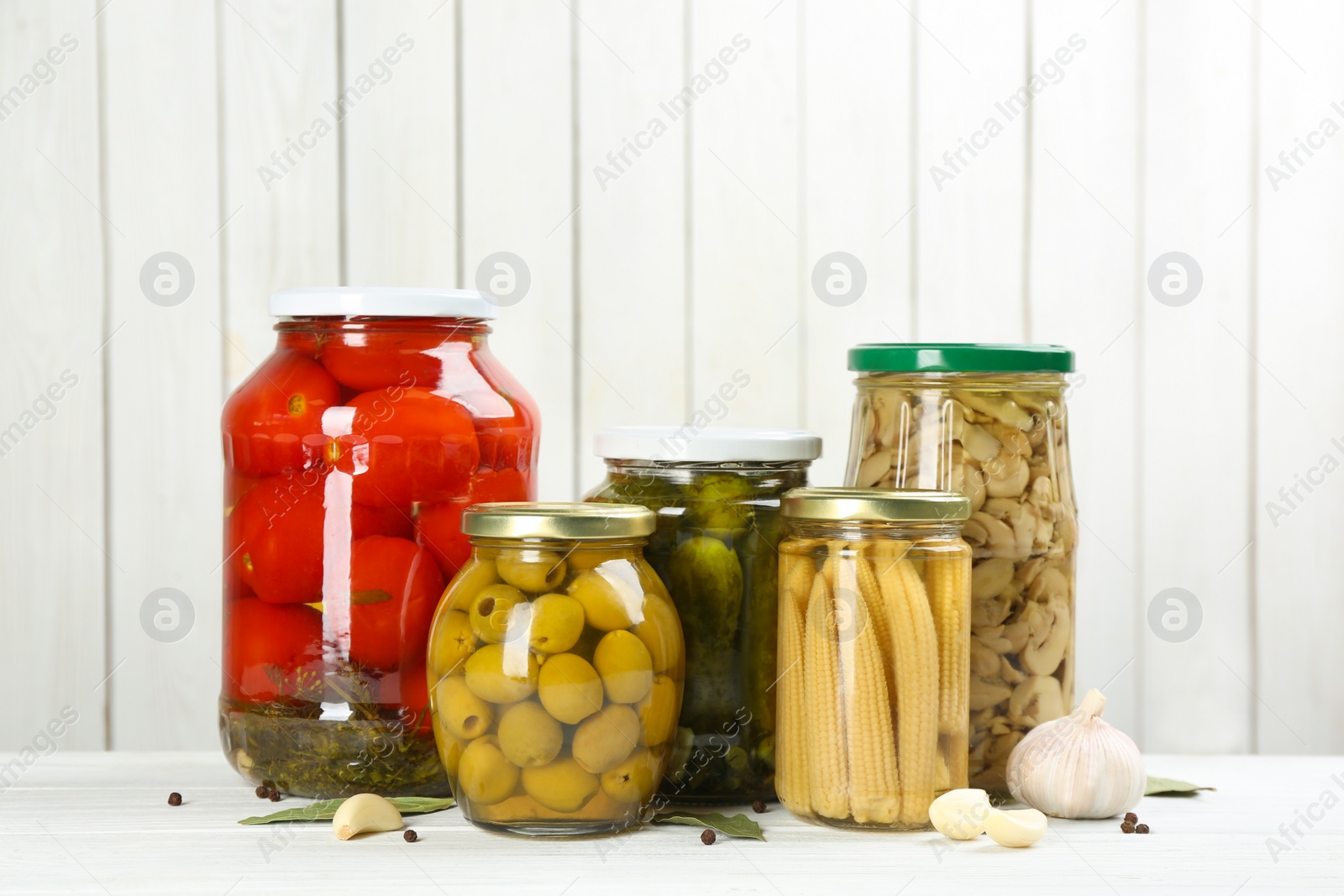 Photo of Glass jars with different pickled vegetables on white wooden background