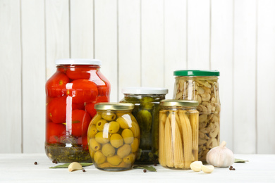 Glass jars with different pickled vegetables on white wooden background