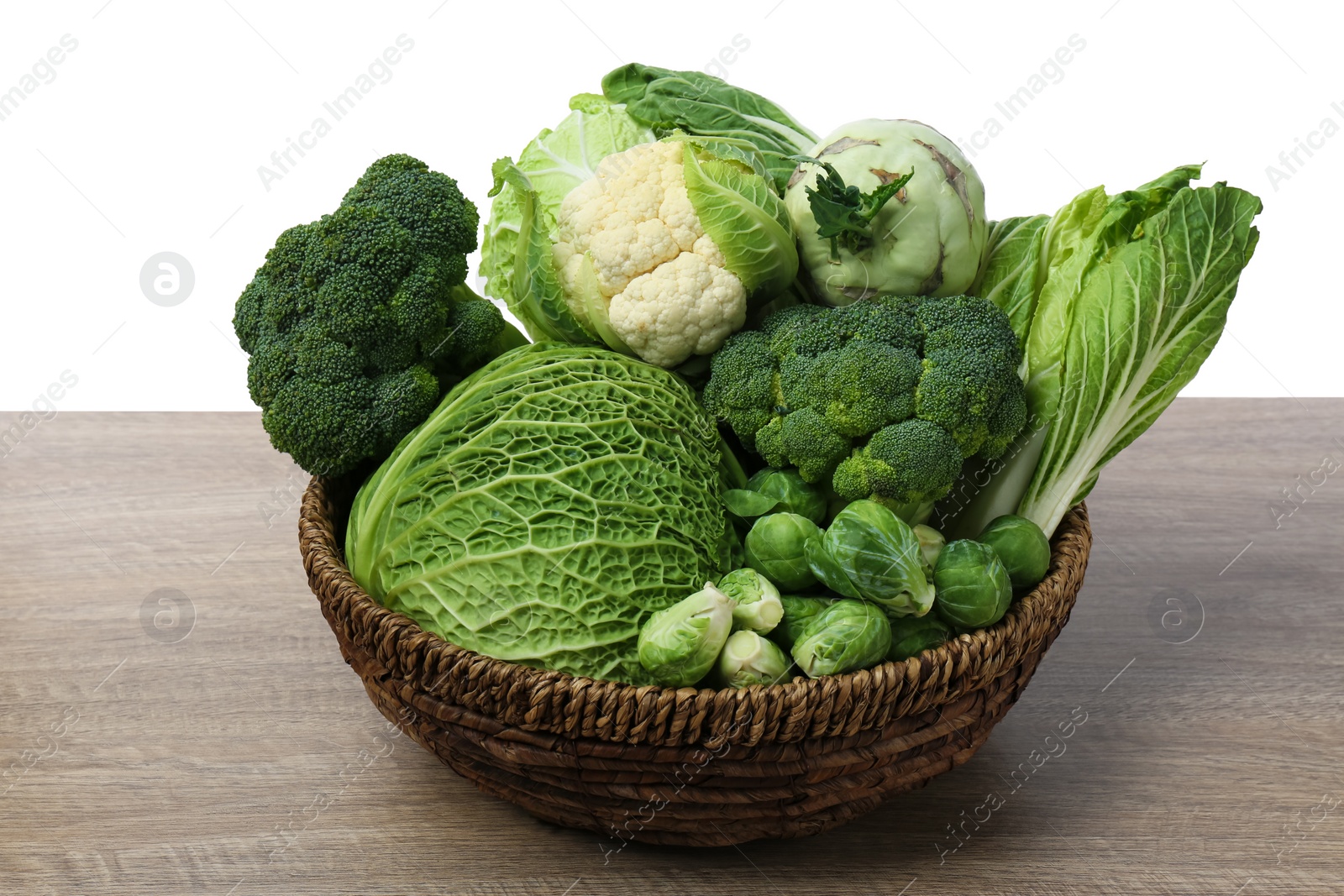 Photo of Wicker bowl with different types of fresh cabbage on wooden table against white background