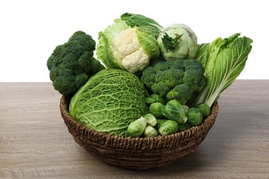 Photo of Wicker bowl with different types of fresh cabbage on wooden table against white background