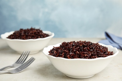 Bowls with delicious cooked brown rice on white table