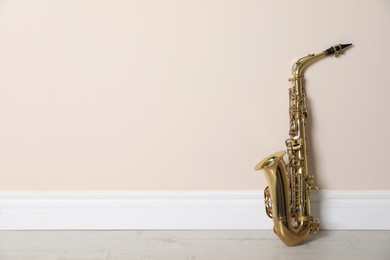 Photo of Beautiful saxophone on floor near beige wall indoors, space for text