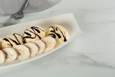 Photo of Delicious banana ice cream with chocolate topping and fresh fruit on white marble table, closeup