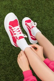 Woman wearing classic old school sneakers on green grass outdoors, above view