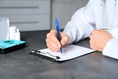 Photo of Doctor writing at table with different medical objects, closeup