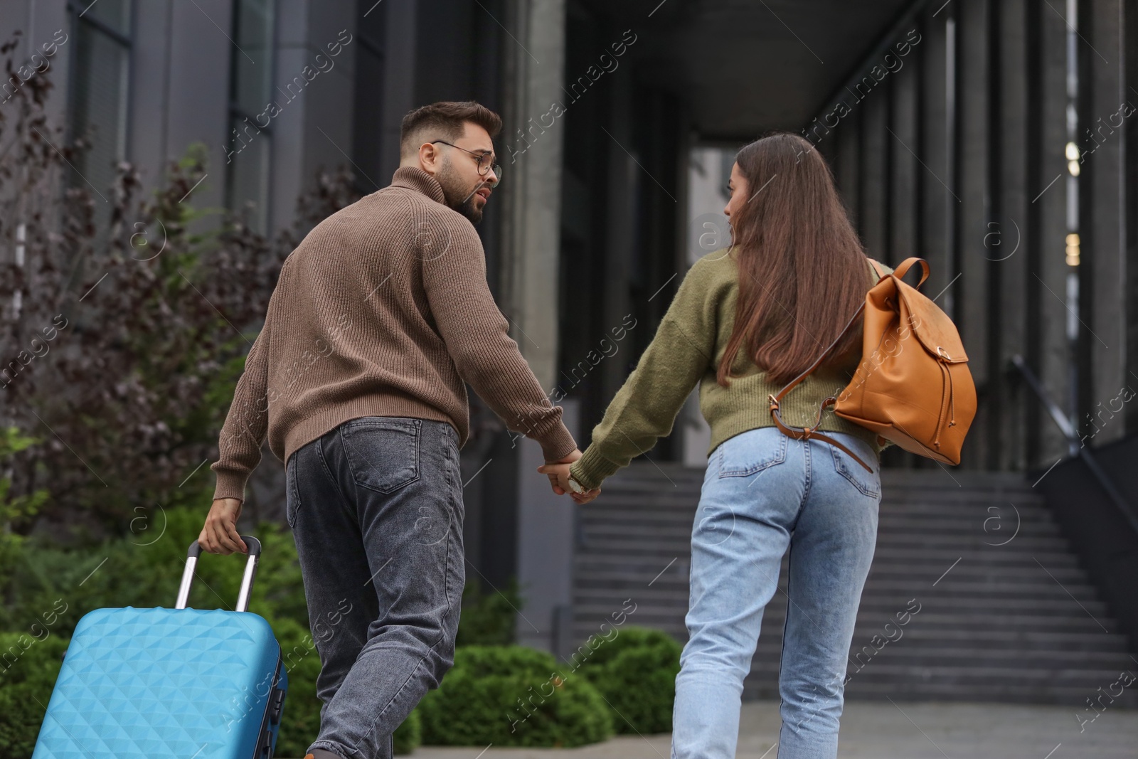 Photo of Being late. Worried couple running towards building outdoors, back view